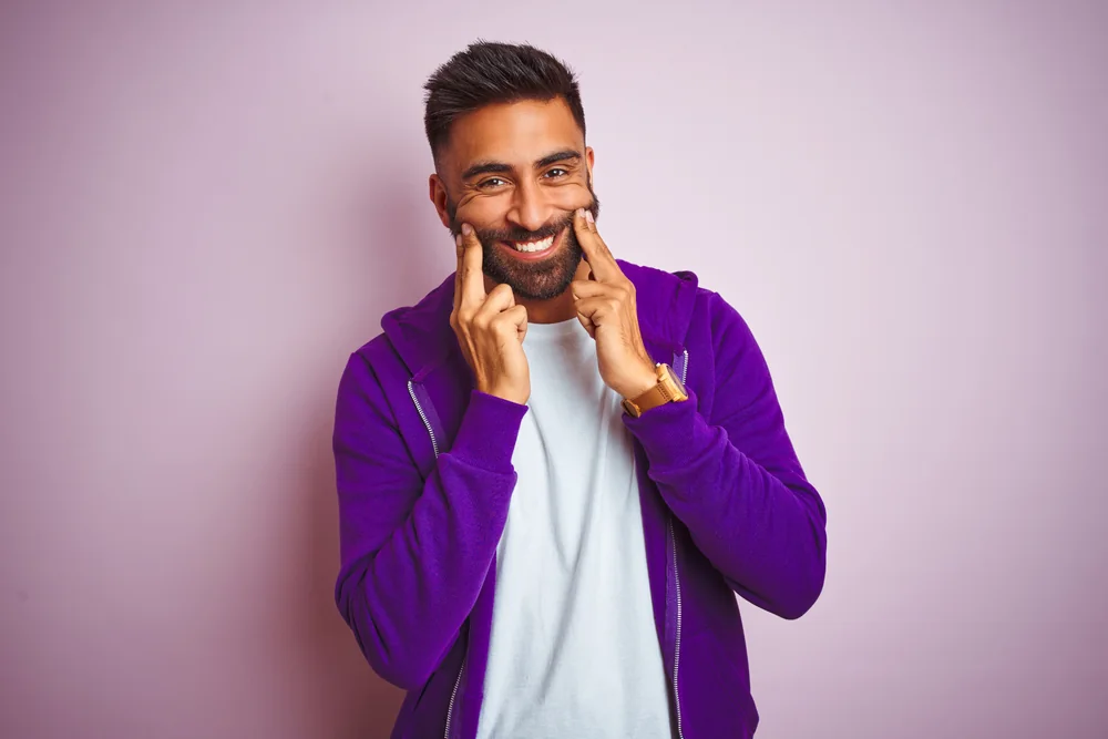 Man smiling and pointing to his teeth after dental crown treatment