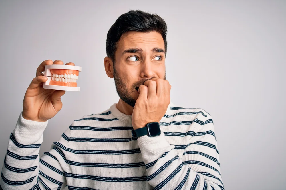 Man looking anxious while holding a model of teeth